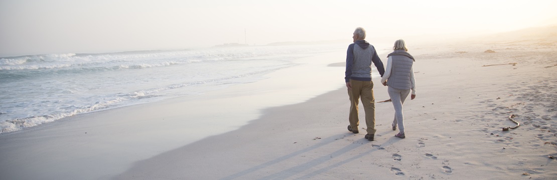 Rearview of retired couple walking on the beach.