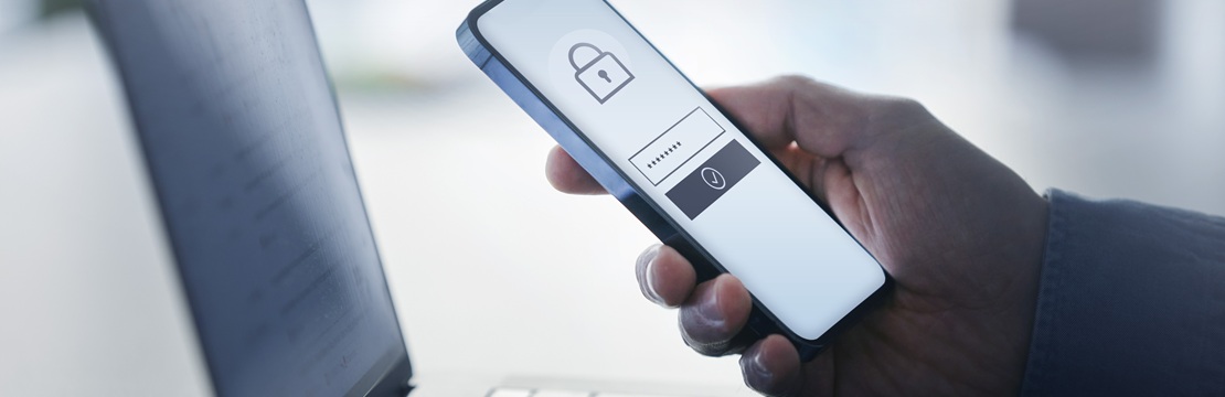Hand holding a smartphone with a lock icon beside a laptop, illustrating cybersecurity and secure authentication.